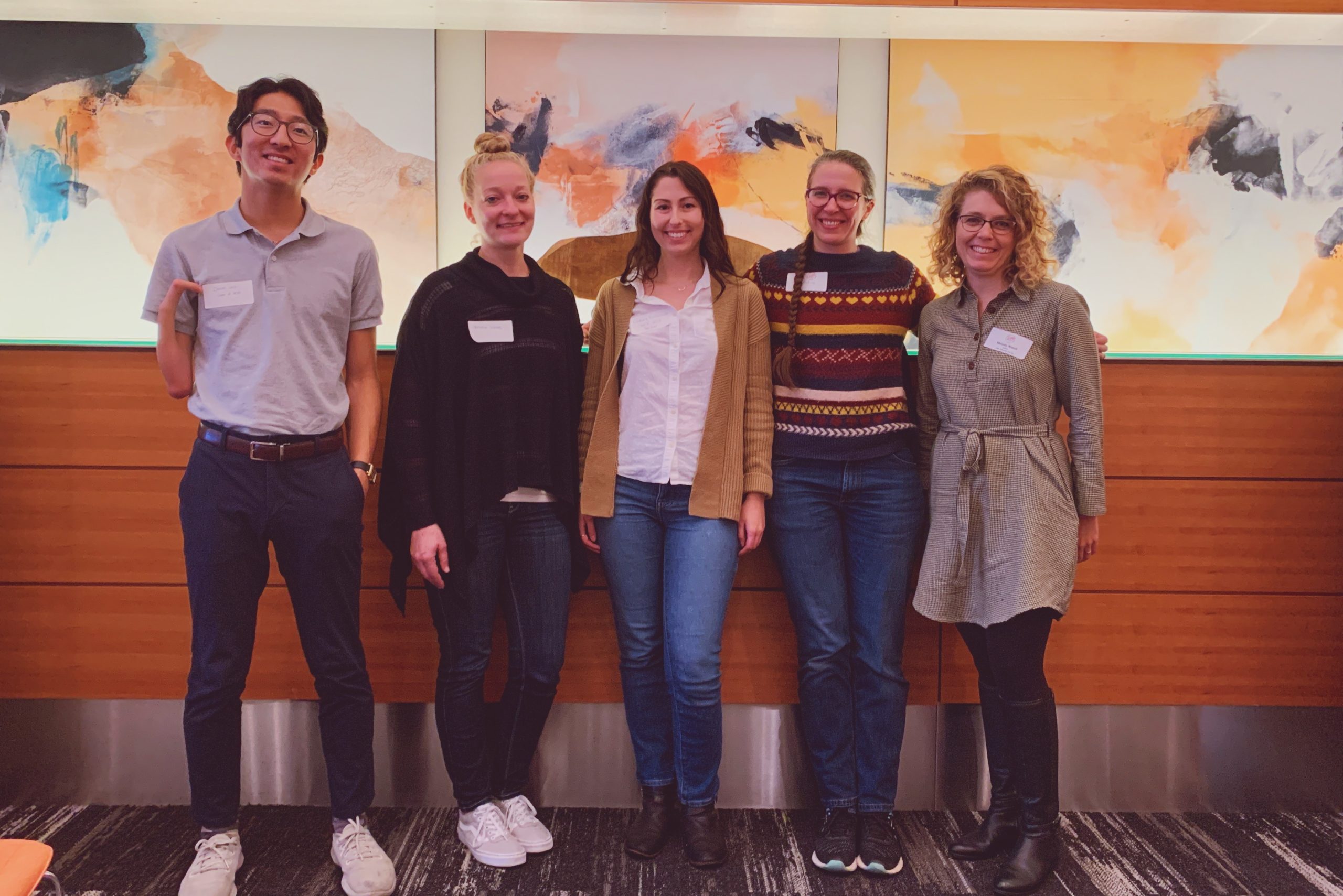 5 people standing in front of 3 paintings in the background.